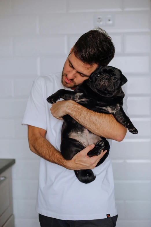 a man in white shirt holding two pug dogs