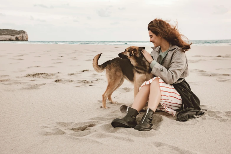 a woman sitting on a beach with a dog
