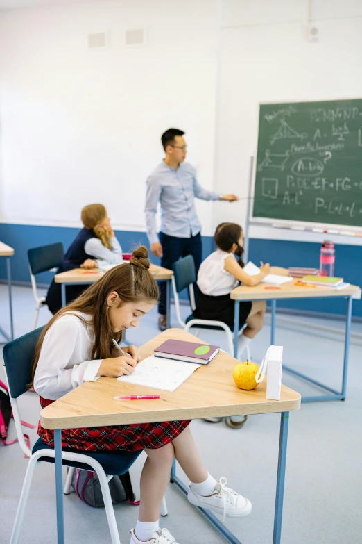 a group of s are sitting at desks in front of a man