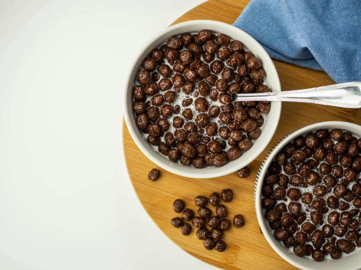 two bowls filled with chocolate cereal sit on a  board