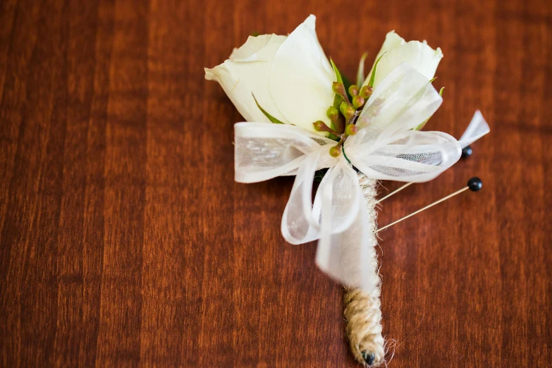 a white rose boutonnier on a table with white ribbon