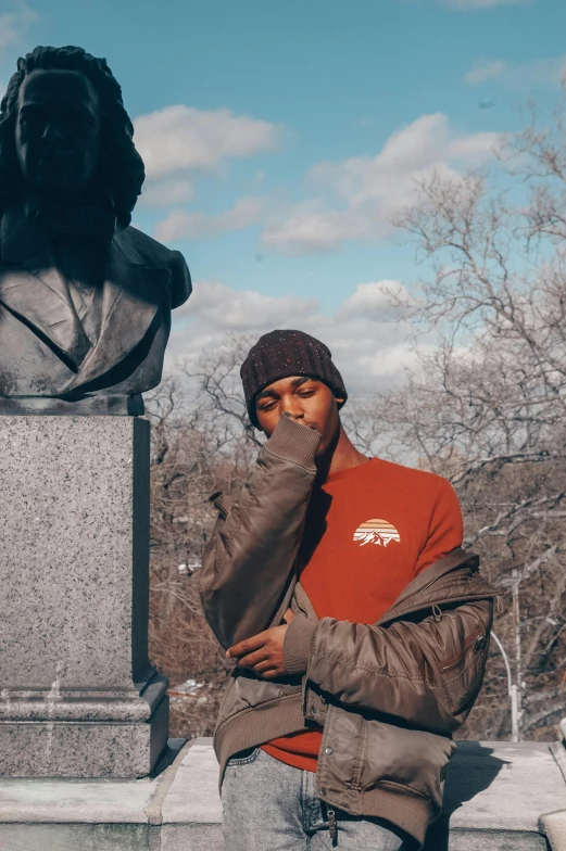 a young man poses near a statue in the background