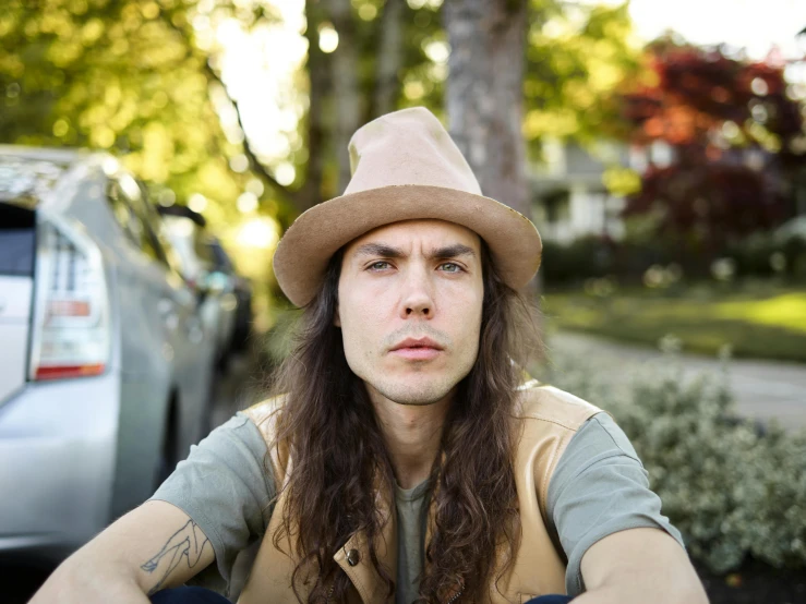 a man sitting down with a hat on and long hair