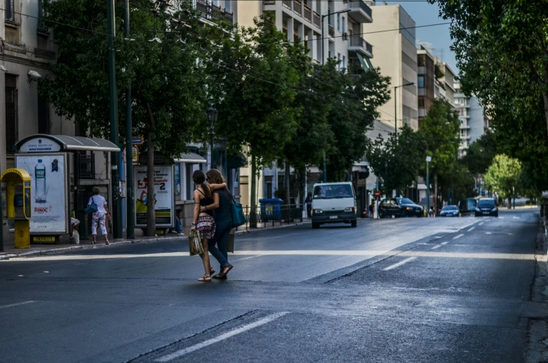 two people walking down a road under tall buildings