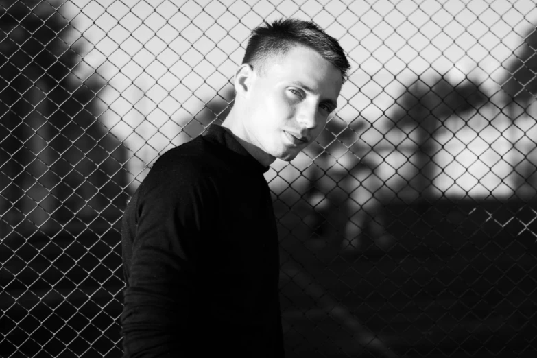 the man looks down on his left eye as he leans against a fence