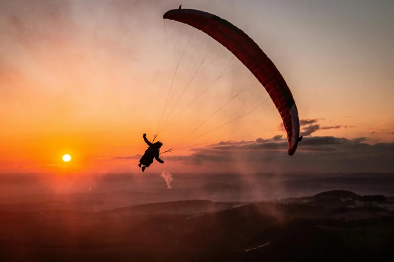 a person in the air with a parachute during a sunset