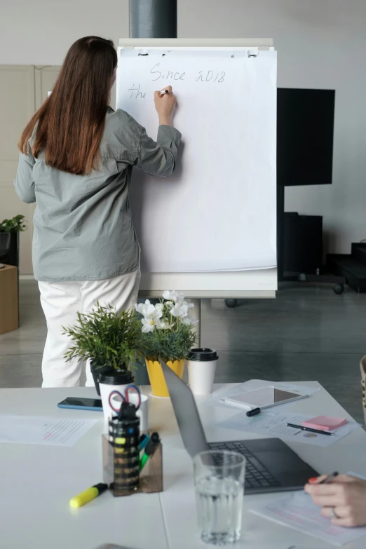 a person writing on a board while another person uses a laptop on a table