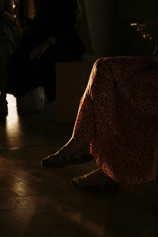 woman in floral dress sitting with a phone by her foot