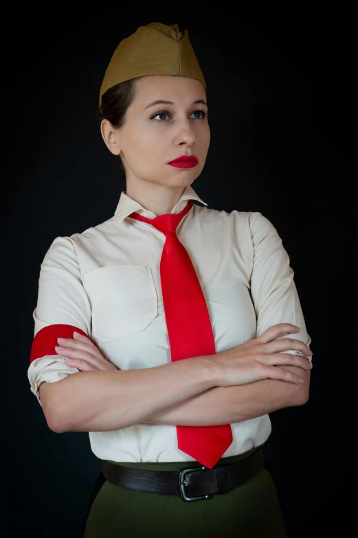 a woman in a short green skirt, white shirt and red tie with a brown hat with her arms folded