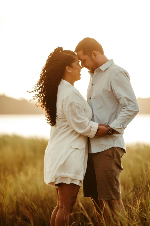 couple in white pose in field with water and grass