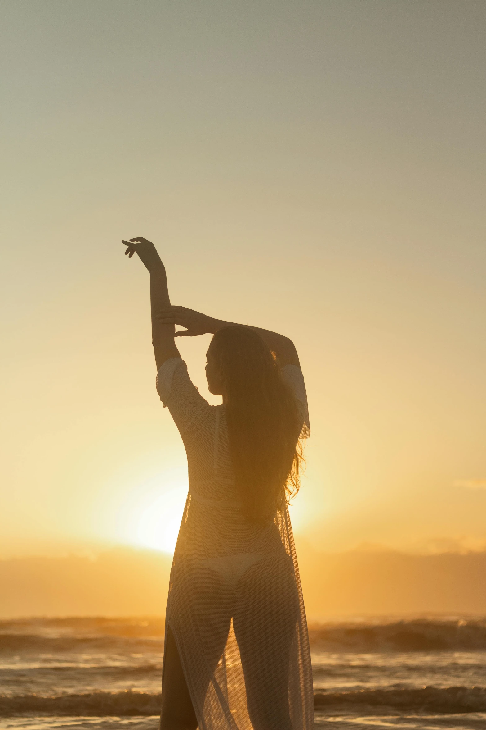 a woman is walking along the beach at sunset