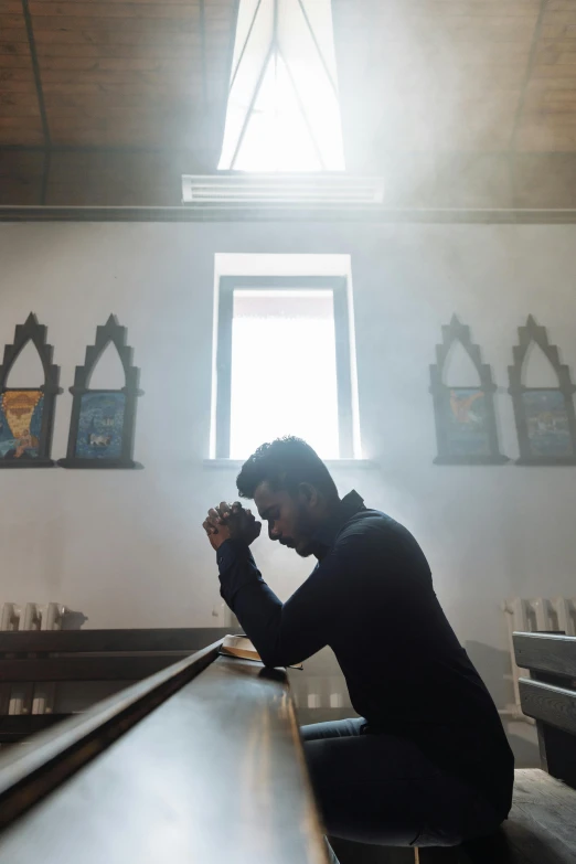 a young man is sitting on a bench and praying