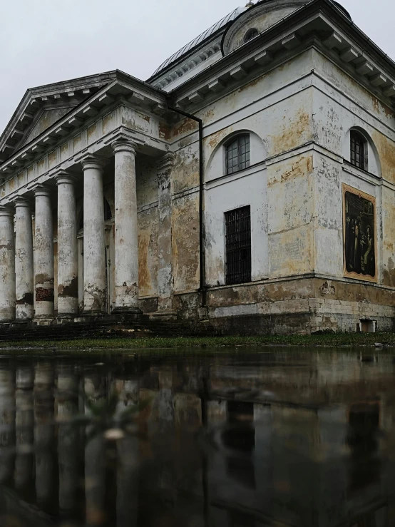 an old white house with pillars is reflected in the still water