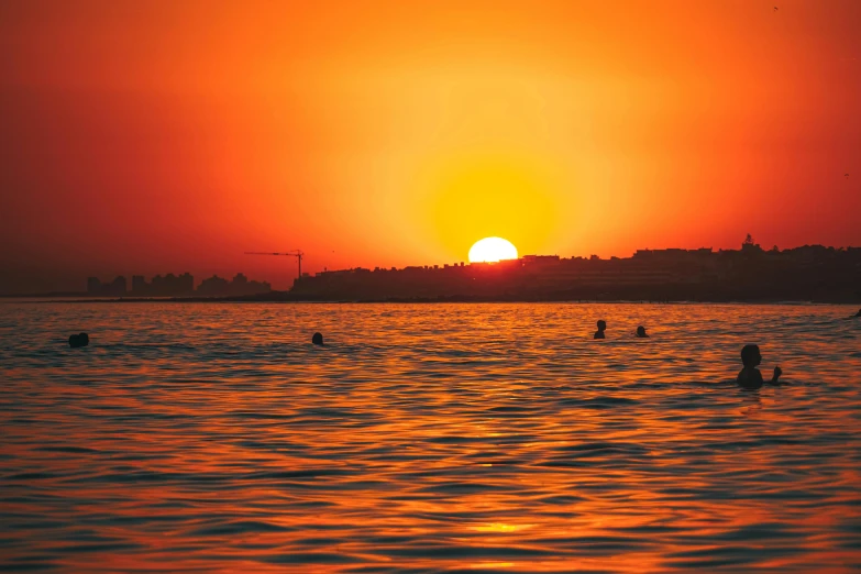 several people are swimming in the ocean at sunset