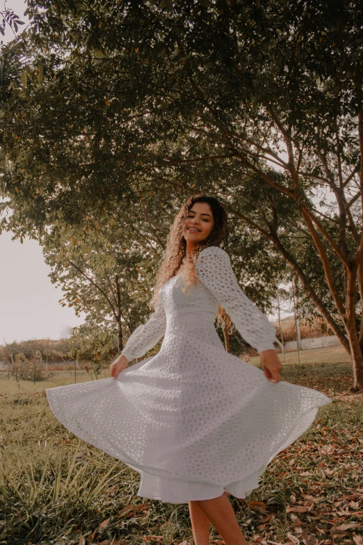 a woman wearing white clothing posing in front of trees