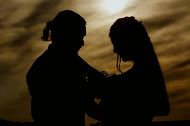 there are two silhouettes against the sky with sun peeking through