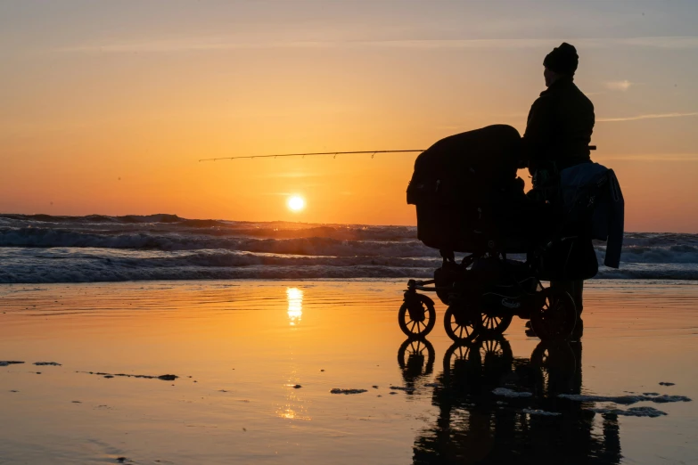 a stroller and a man watch the sun set over the ocean