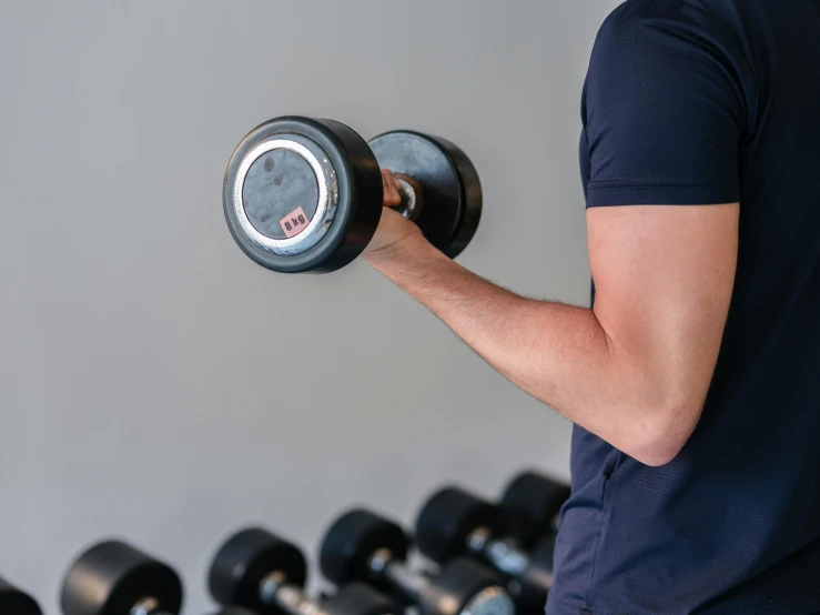 man holding the bar with both hands and dumbbells on the wall in the background