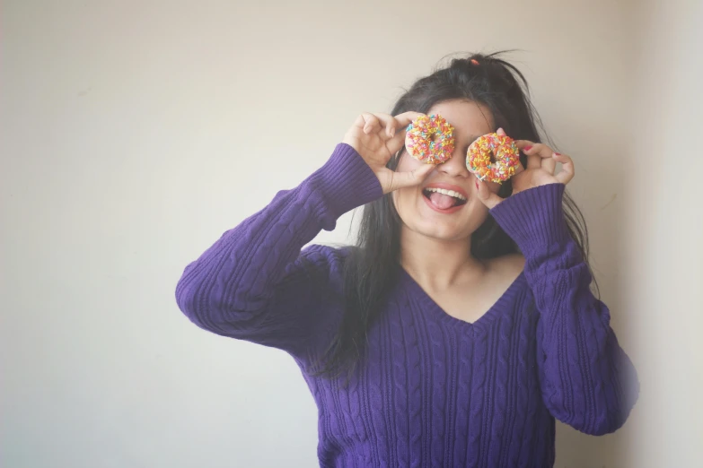 a woman wearing purple holds a doughnut over her eyes