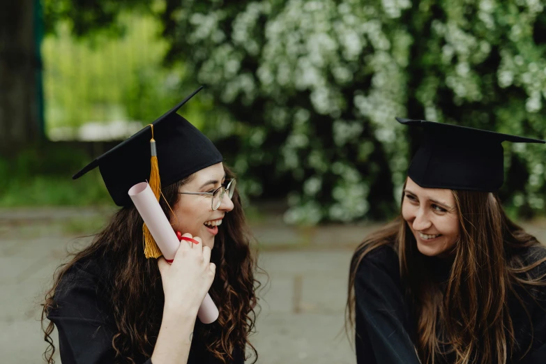 two smiling graduates sitting next to each other in graduation caps and gowns