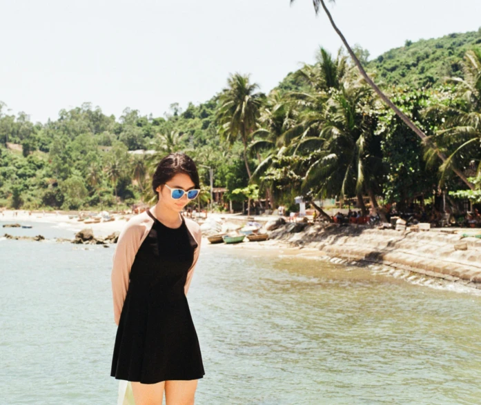 a girl standing on a surfboard with the beach in the background