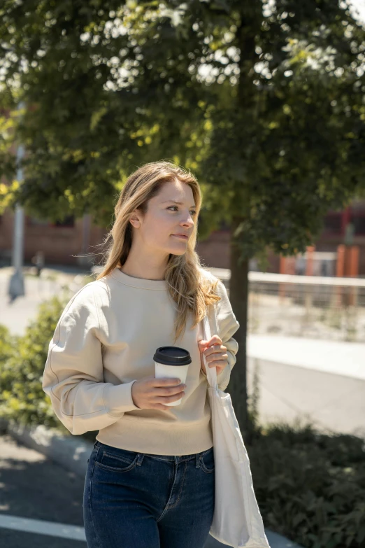 a girl in a tan sweater is holding a cup