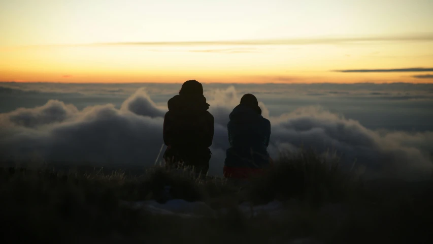 two people on a hill with the sun peeking over the clouds