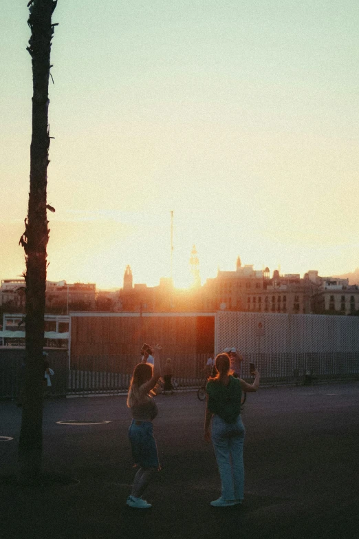 two women are standing in a parking lot watching the sun go down