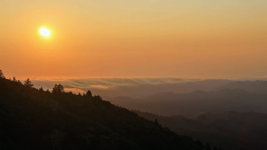 the sun rises over the mountains on a foggy day