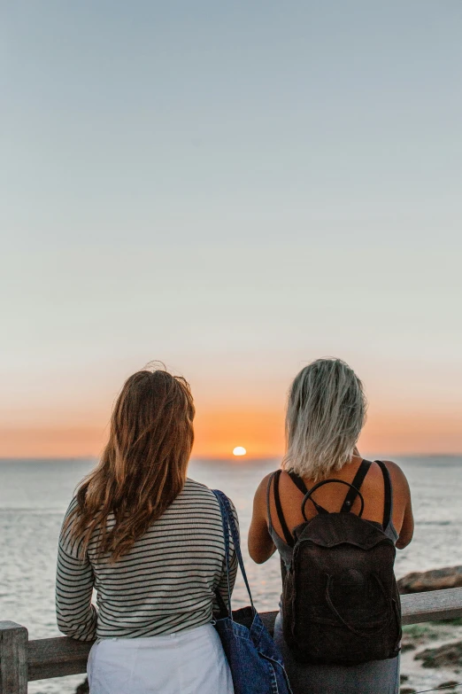 two women sit on a bench looking at the sunset