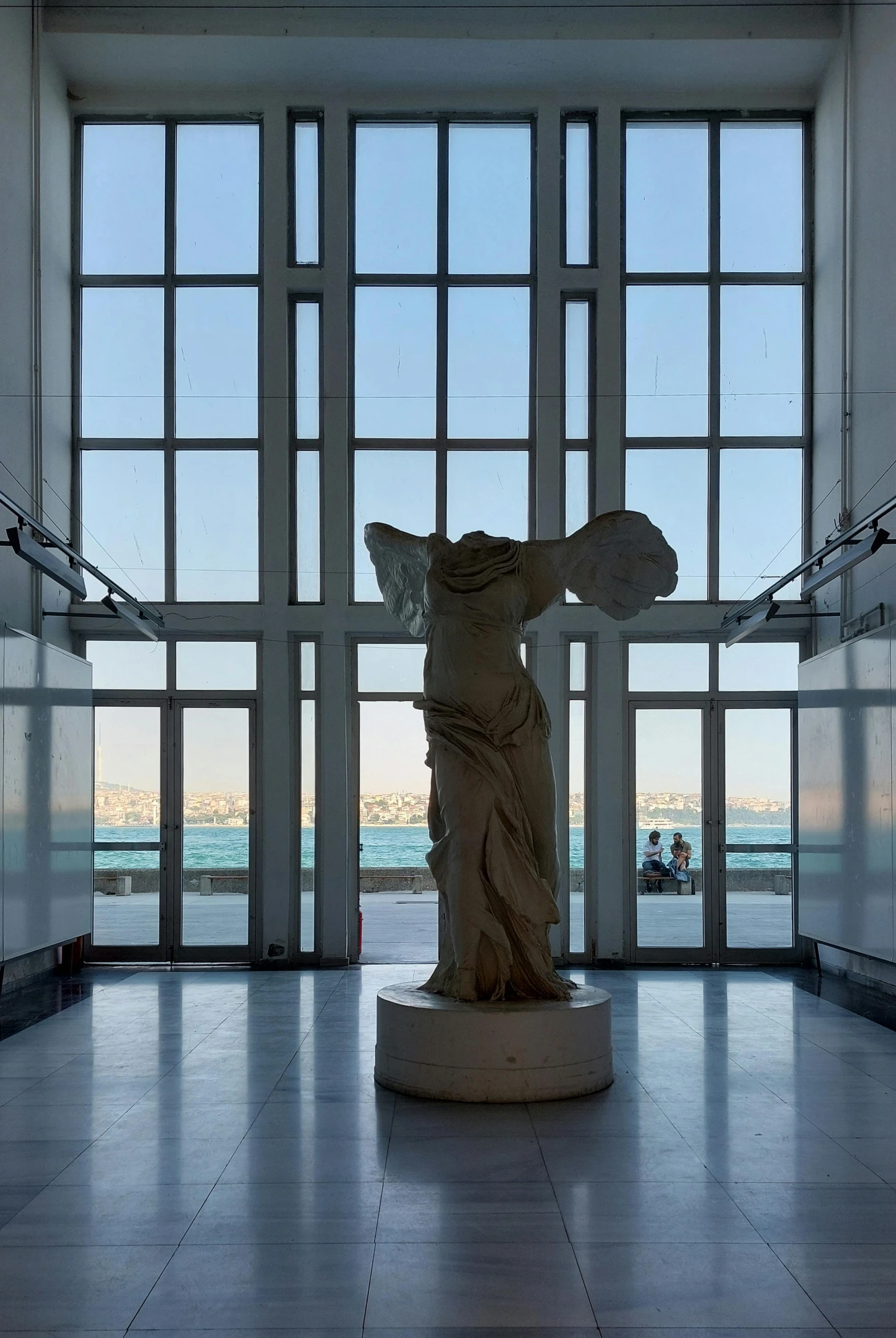 a statue sits inside a museum space in front of large windows