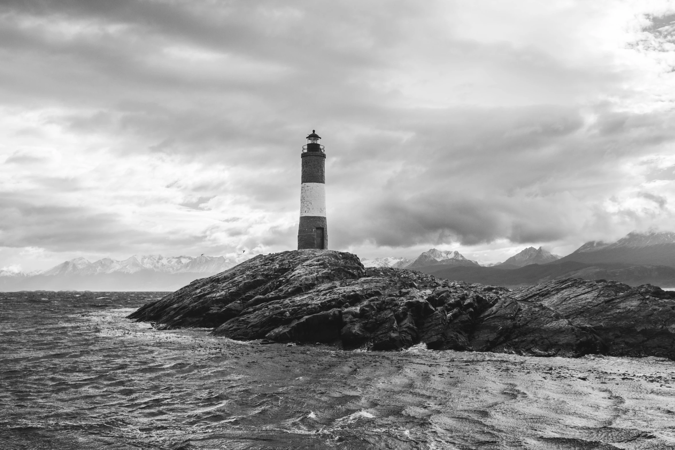 a black and white picture of a lighthouse on a rocky shore