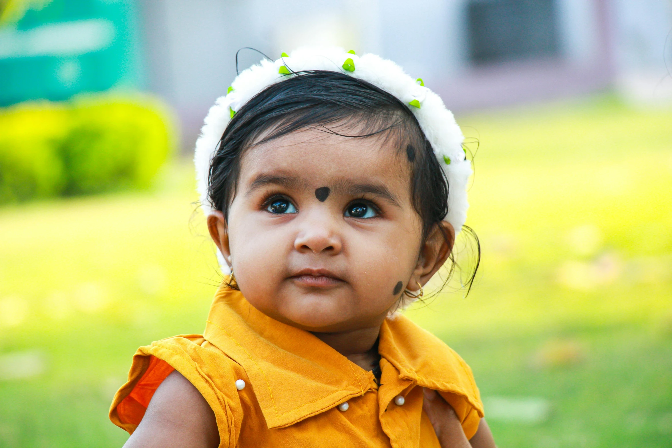 young child in orange shirt sitting outside with grass