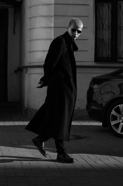 an older man walks down the street, in a long coat