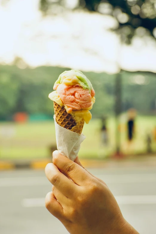 a hand holding an ice cream cone with three different types of ice cream