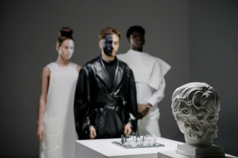 three models looking at a busturine, white sculpture, and black marble