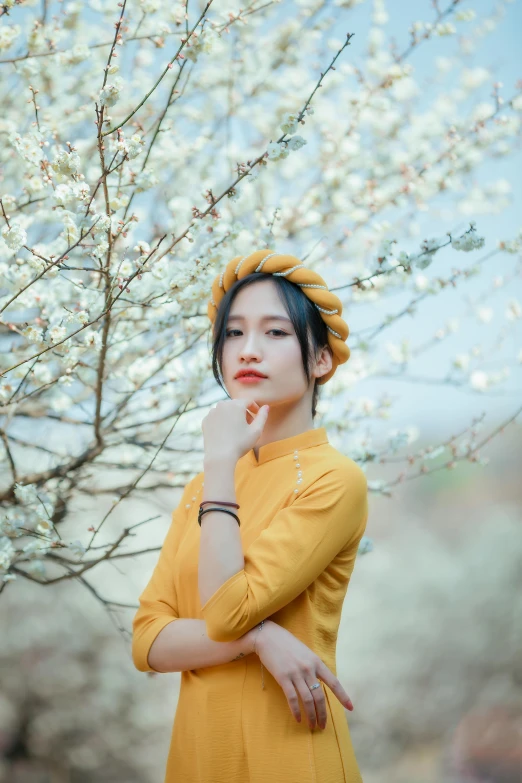 a girl in an orange dress stands by a flowering tree