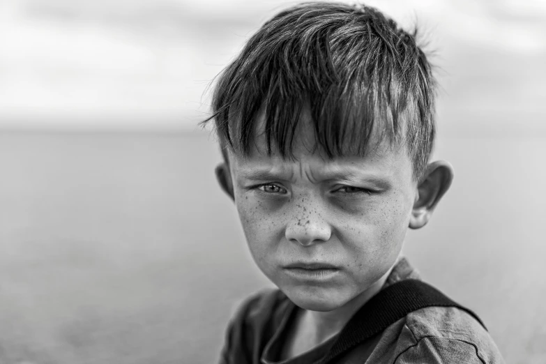 an unhappy little boy looks directly at the camera