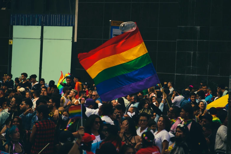 a large rainbow flag in the middle of people in a crowded square