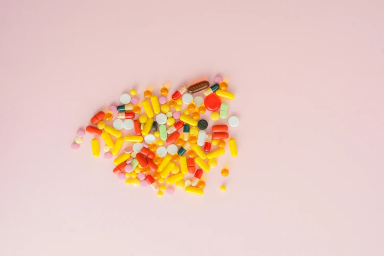 colorful pills are scattered out on a pink surface