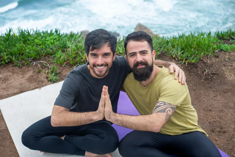 two men sitting on yoga mats smiling for a po