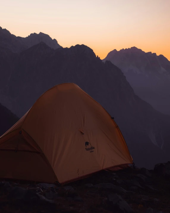 a tent sitting in the middle of a mountain under a sunset