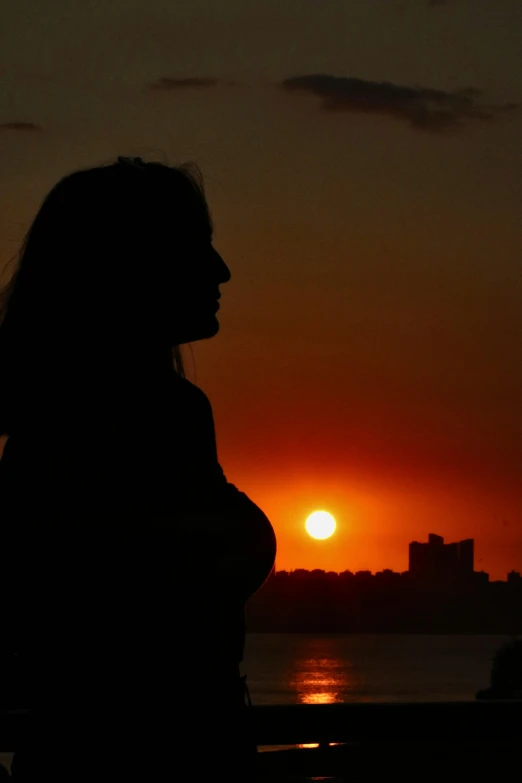 a woman standing in front of a sunset and clouds