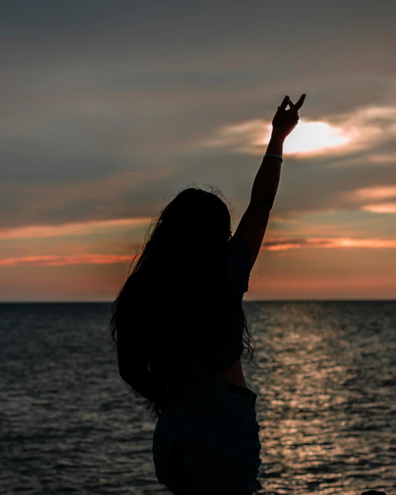 a silhouette of a person near the ocean reaching out to shake the sun