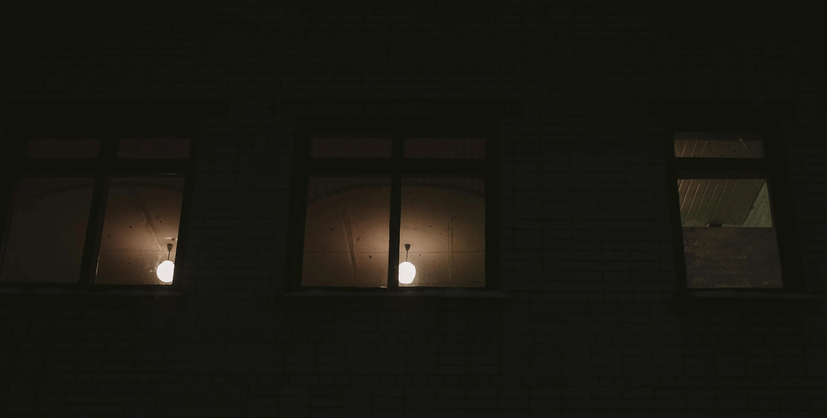 three lit windows at night showing two people on one