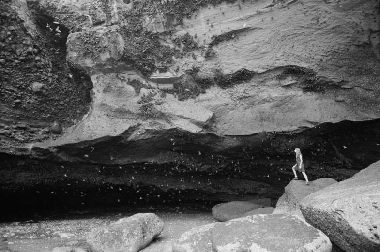a person walks on a large rock at the entrance to a cave