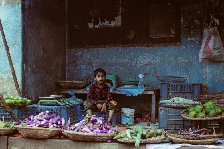 a boy sitting in front of vegetables on display