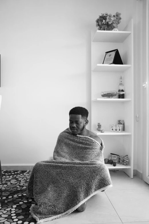 a woman wrapped in blanket sitting on floor next to shelves