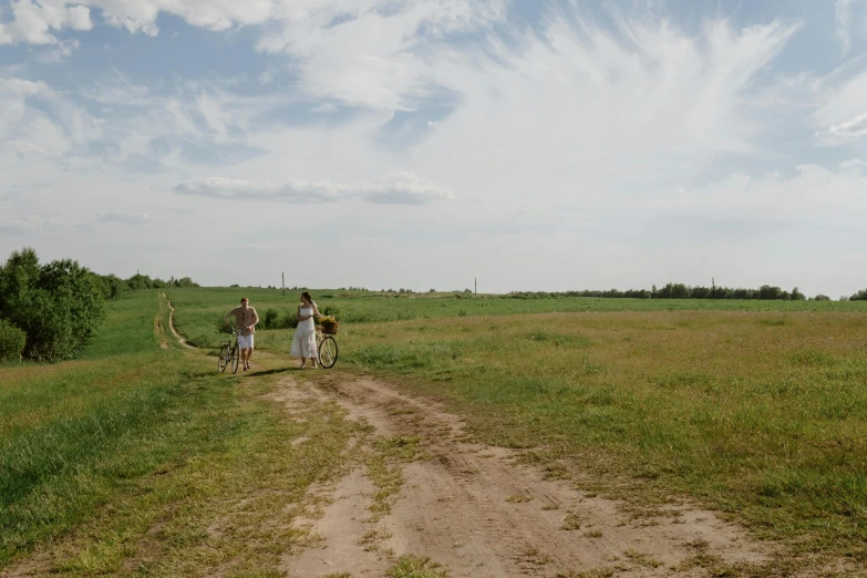 two people walking on dirt road with green grass