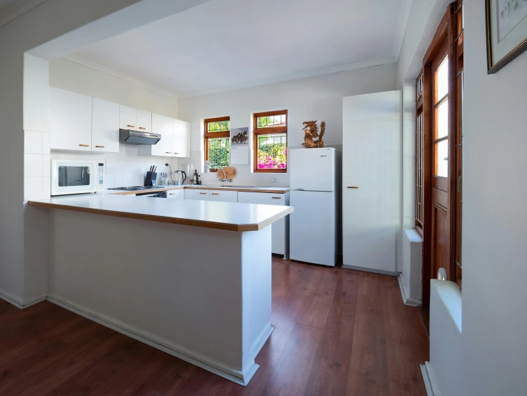 an empty kitchen with all white appliances and wood floors